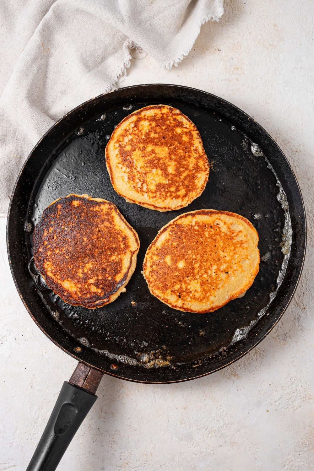Three cooked pancakes in a cast iron skillet.