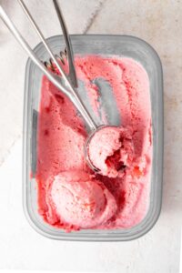 An ice cream scoop in a tub of strawberry cottage cheese ice cream