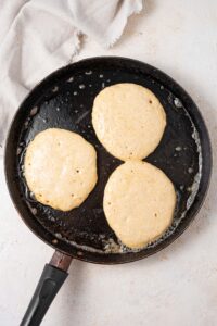 Three partially cooked pancakes on a cast iron skillet.