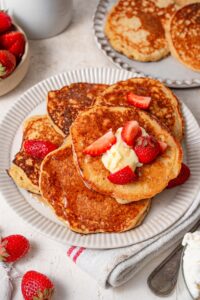 Five cottage cheese pancakes on a plate, topped with butter and strawberry slices.