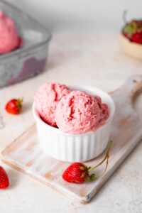 Strawberry cottage cheese ice cream in a bowl, surrounded by fresh strawberries.