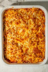 A casserole dish of baked spaghetti topped with golden melted cheese.