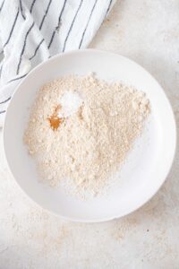 Oat flour, baking powder, and cinnamon in a large white bowl.
