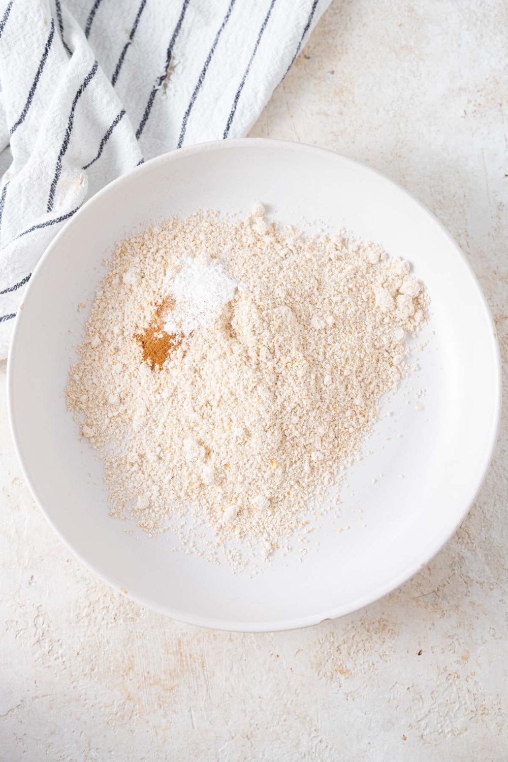 Oat flour, baking powder, and cinnamon in a large white bowl.