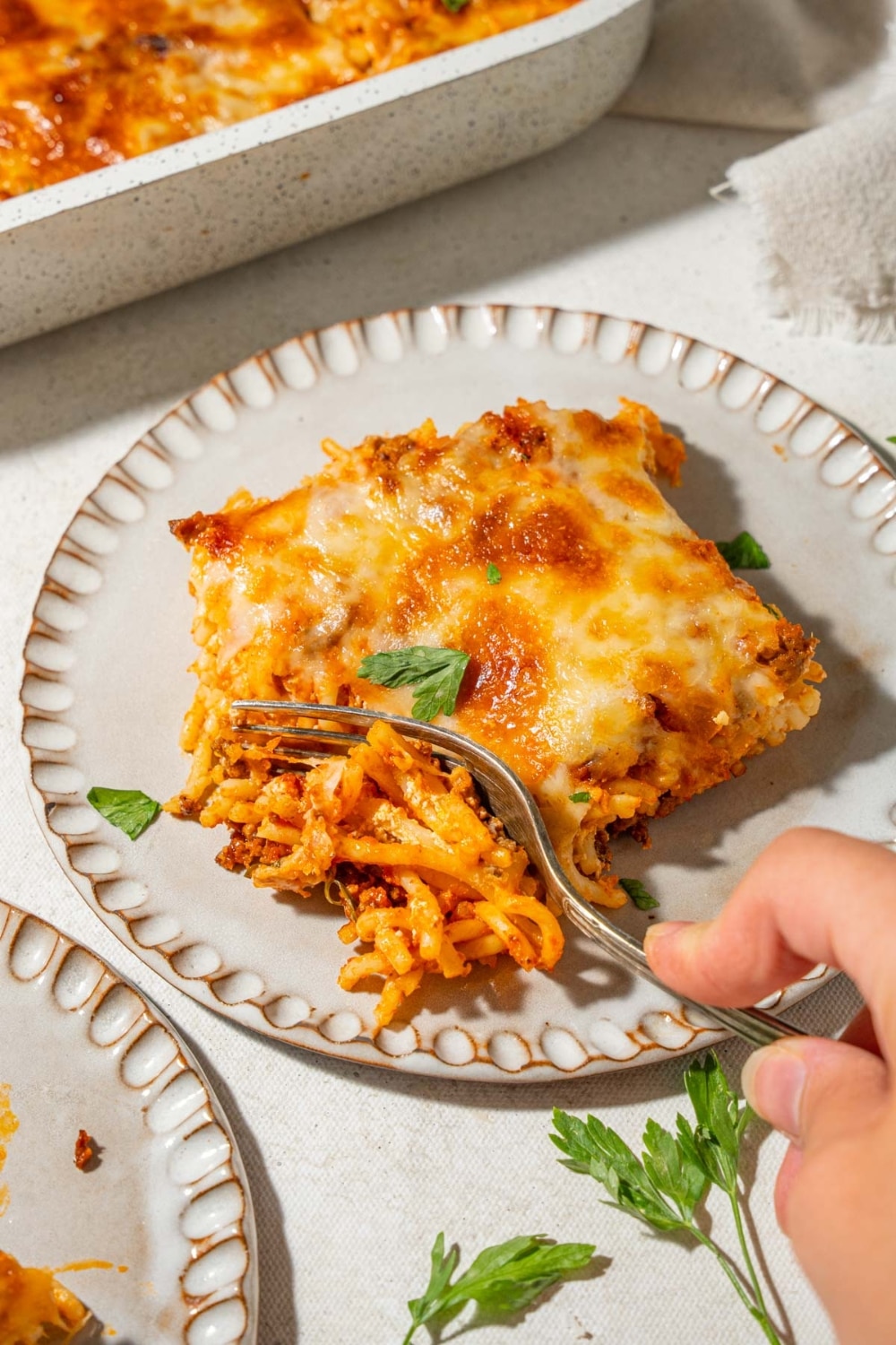 Cutting into a slice of baked spaghetti topped with herbs on a plate.
