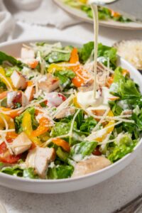Dressing being poured onto a chicken Caesar salad.
