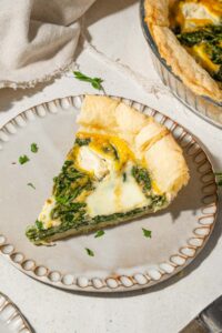 A slice of spinach quiche with whipped cottage cheese topping on a plate, garnished with fresh herbs.