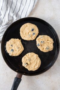 Four uncooked cottage cheese banana blueberry pancakes in a skillet with oil.
