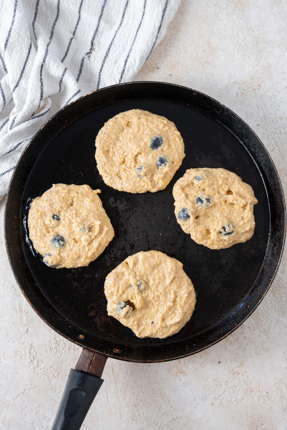 Four uncooked cottage cheese banana blueberry pancakes in a skillet with oil.