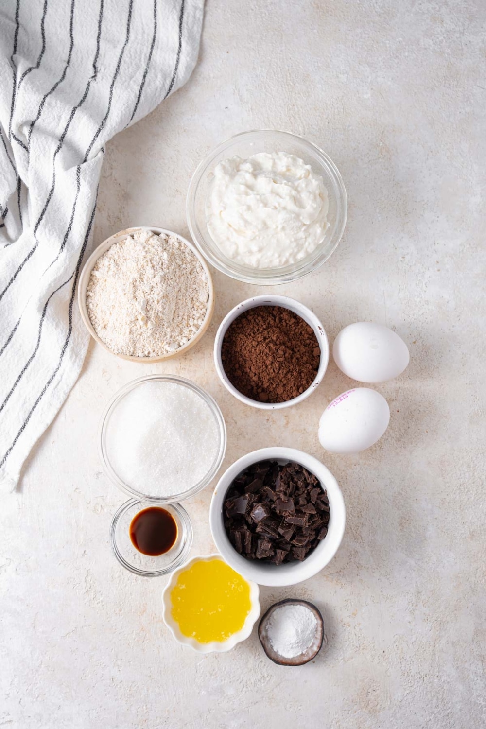 Bowls of cottage cheese, oat flour, cocoa powder, powdered allulose, baking powder, chocolate chunks, vanilla extract, and melted butter, and two eggs.