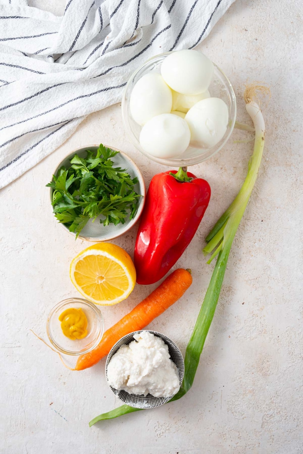 Hardboiled eggs, fresh parsley, a red bell pepper, a stalk of green onion, a sliced lemon, a small carrot, and small bowls of mustard and cottage cheese.