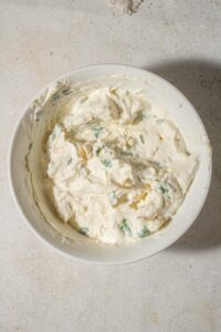 Sour cream, cream cheese, cottage cheese, parmesan cheese, and chopped parsley mixed together in a bowl.