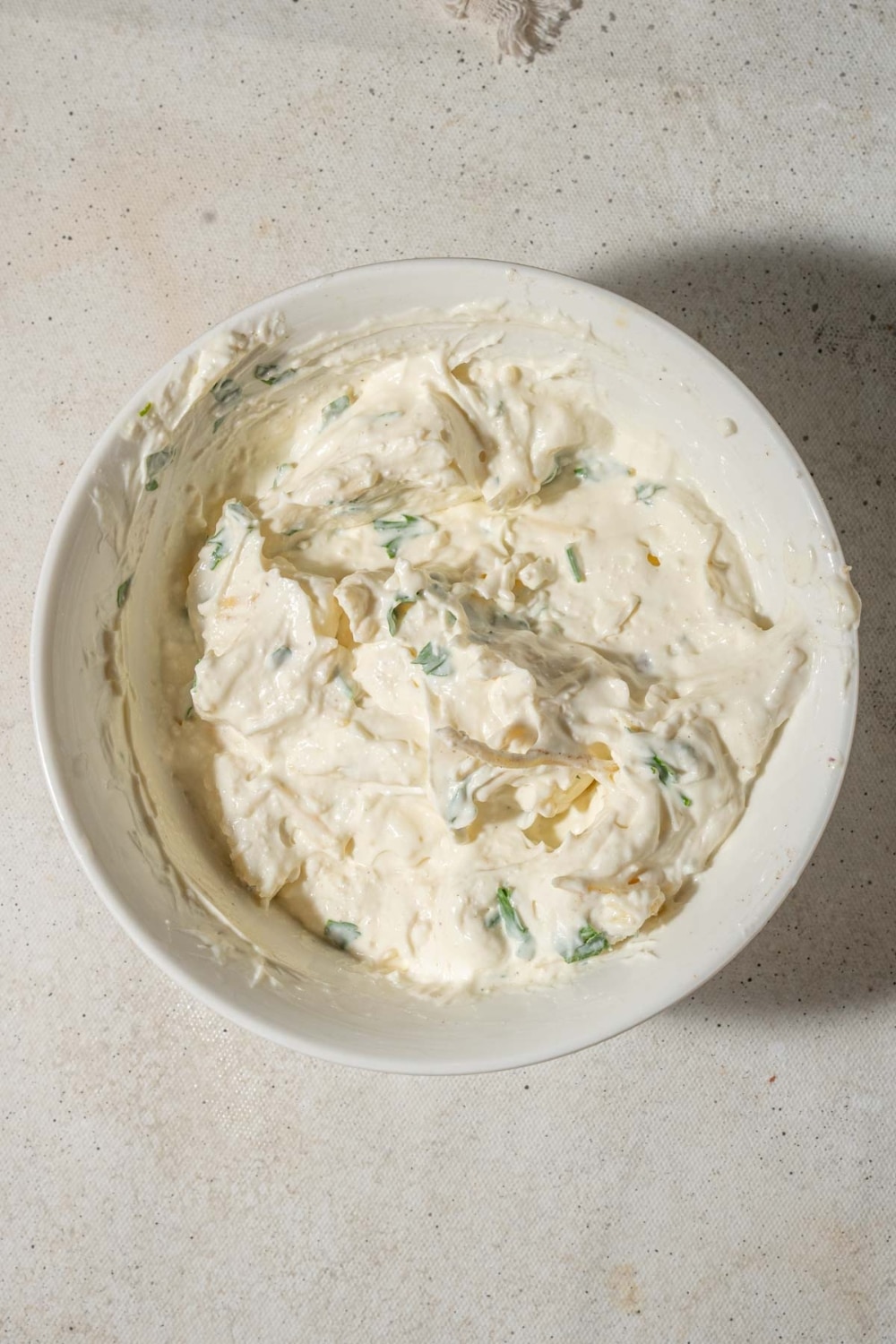 Sour cream, cream cheese, cottage cheese, parmesan cheese, and chopped parsley mixed together in a bowl.