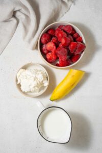 Bowls of frozen strawberries and cottage cheese, a banana, and a mini pitcher of almond milk.