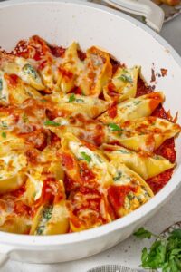 Spinach and cottage cheese stuffed pasta shells in marinara sauce in a white pot.