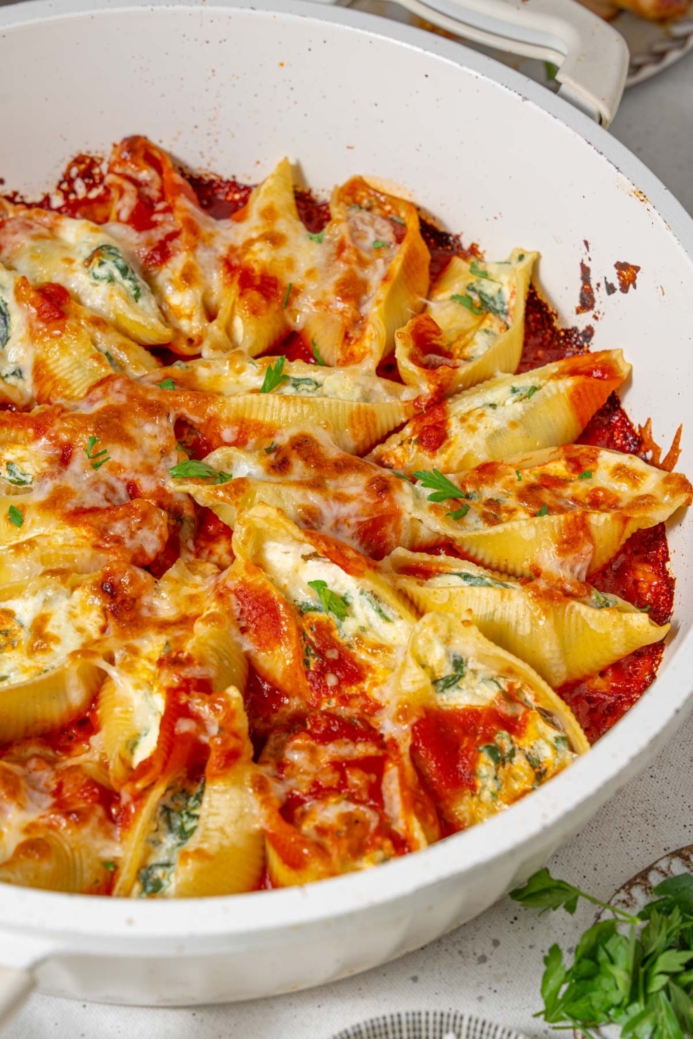 Spinach and cottage cheese stuffed pasta shells in marinara sauce in a white pot.