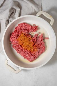 Raw ground beef and spices in a white pot.