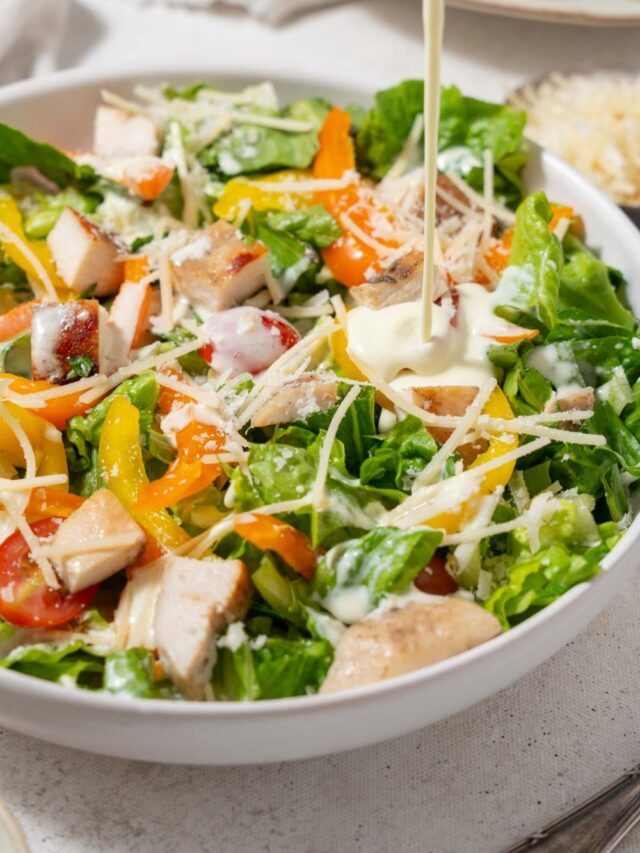 Dressing being poured onto a chicken Caesar salad.