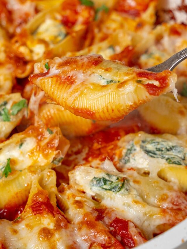Lifting a spinach and cottage cheese stuffed pasta shell from a pot with a fork.