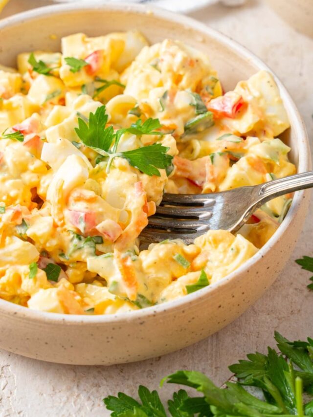 A fork digging into a bowl of cottage cheese egg salad garnished with fresh parsley.