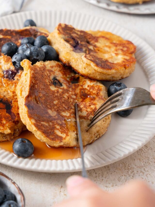 Cutting into cottage cheese banana blueberry pancakes with a fork and knife.