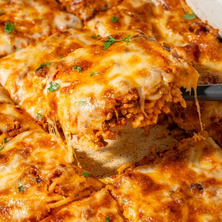 Lifting a slice of baked spaghetti from a casserole dish.