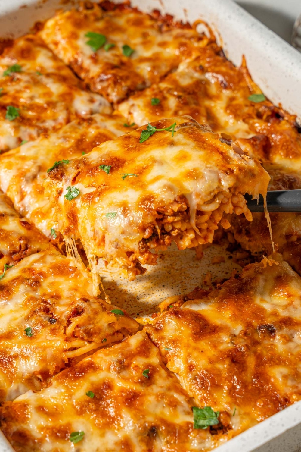 Lifting a slice of baked spaghetti from a casserole dish.