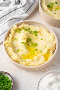 A bowl of cottage cheese mashed potatoes garnished with chives and melted butter.