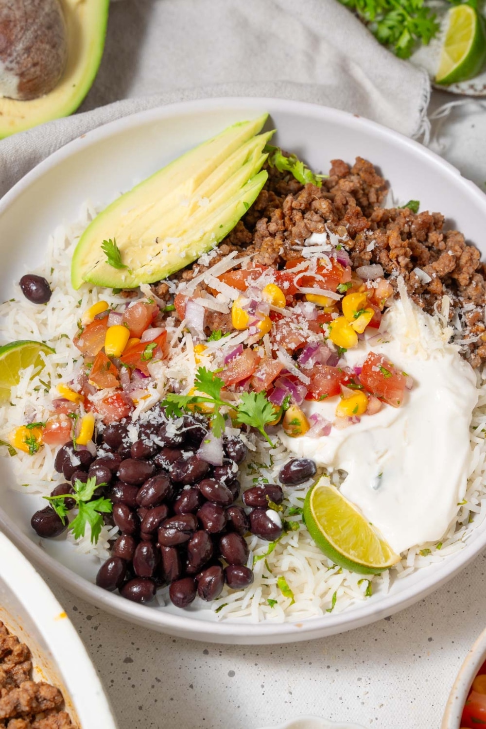 A taco bowl with taco meat, sliced avocado, rice, veggies, beans, and cottage cheese sauce.