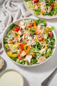 Chicken Caesar salad in a bowl topped with grated parmesan cheese and dressing.