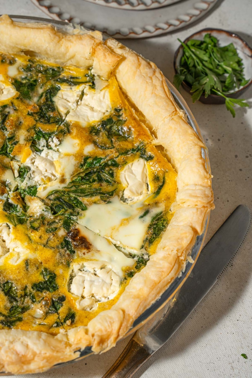 A sliced spinach quiche with whipped cottage cheese and fresh herbs.