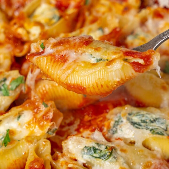 Lifting a spinach and cottage cheese stuffed pasta shell from a pot with a fork.