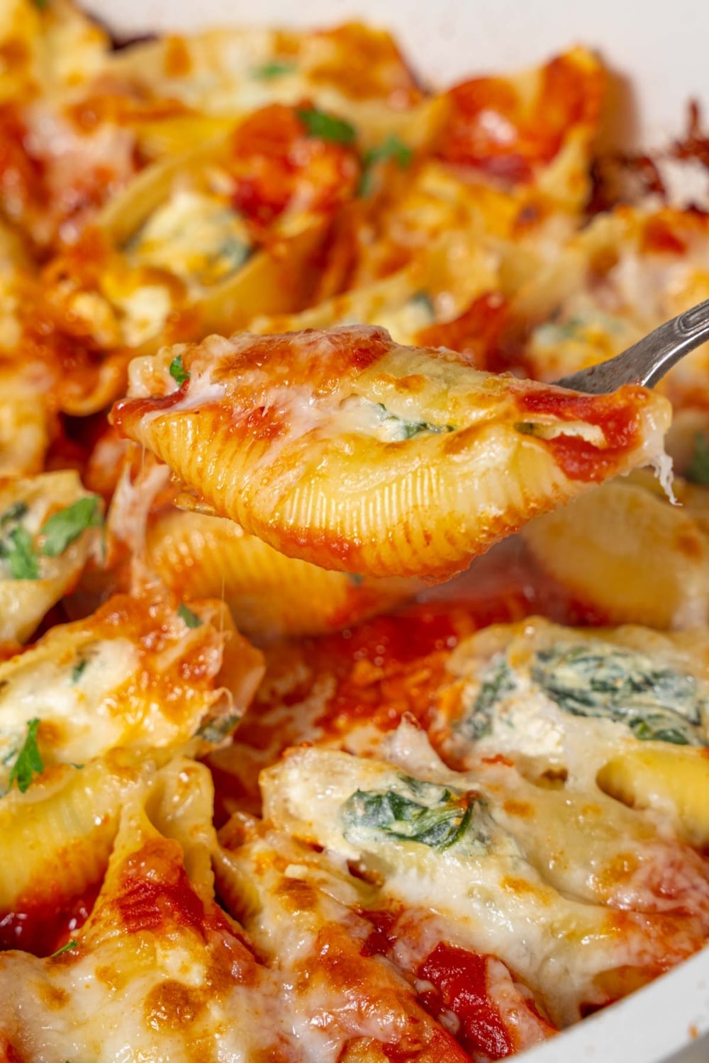 Lifting a spinach and cottage cheese stuffed pasta shell from a pot with a fork.