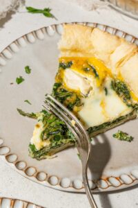 Cutting into a slice of spinach cottage cheese quiche with a fork.