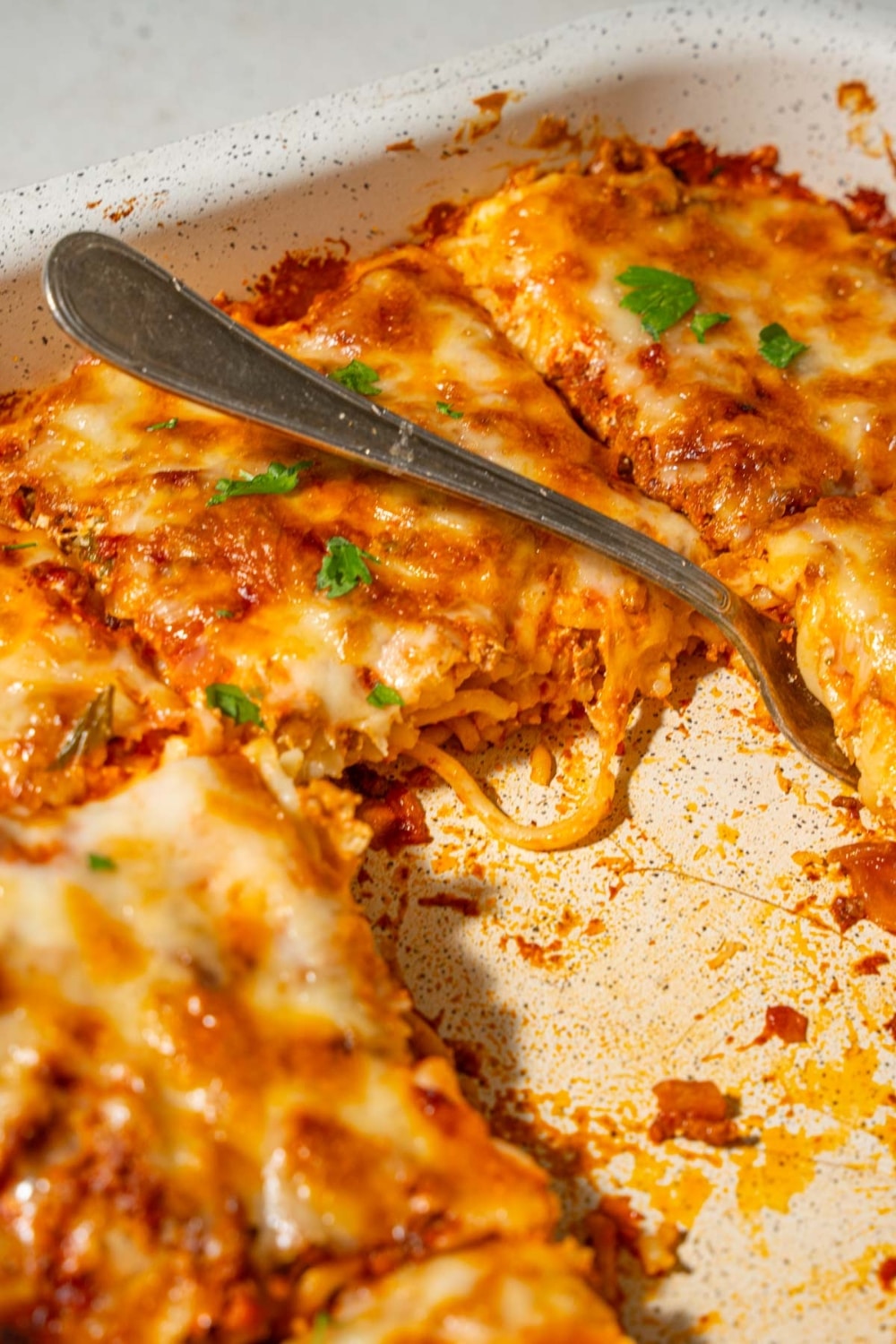 A casserole dish of million dollar spaghetti with some slices taken out and a fork laying in the center.