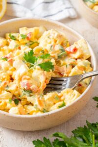 A fork digging into a bowl of cottage cheese egg salad garnished with fresh parsley.