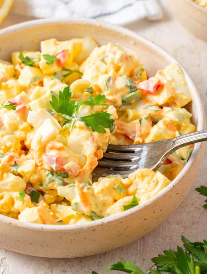 A fork digging into a bowl of cottage cheese egg salad garnished with fresh parsley.