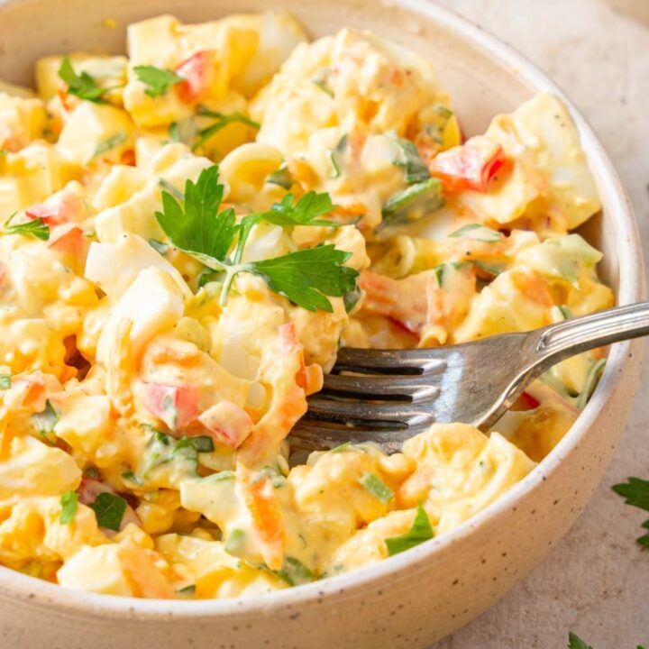 A fork digging into a bowl of cottage cheese egg salad garnished with fresh parsley.