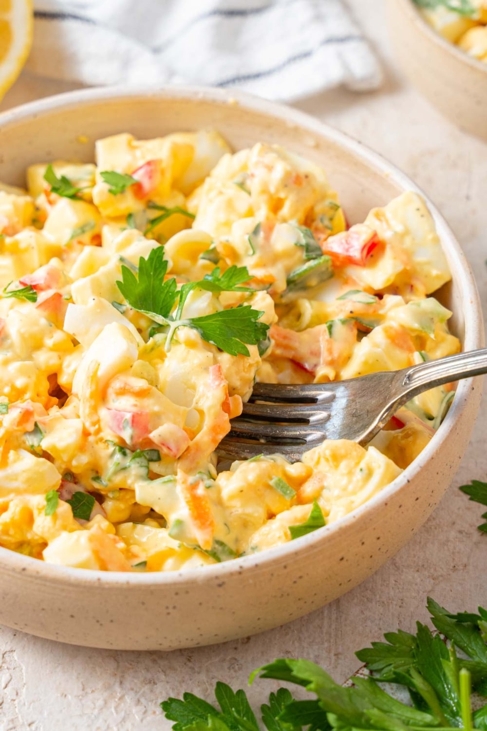 A fork digging into a bowl of cottage cheese egg salad garnished with fresh parsley.