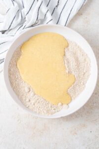 Wet and dry cottage cheese banana blueberry pancake batter ingredients unmixed in a white bowl.
