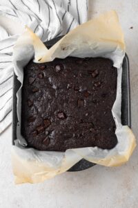 Freshly baked cottage cheese brownies in a parchment paper-lined pan.