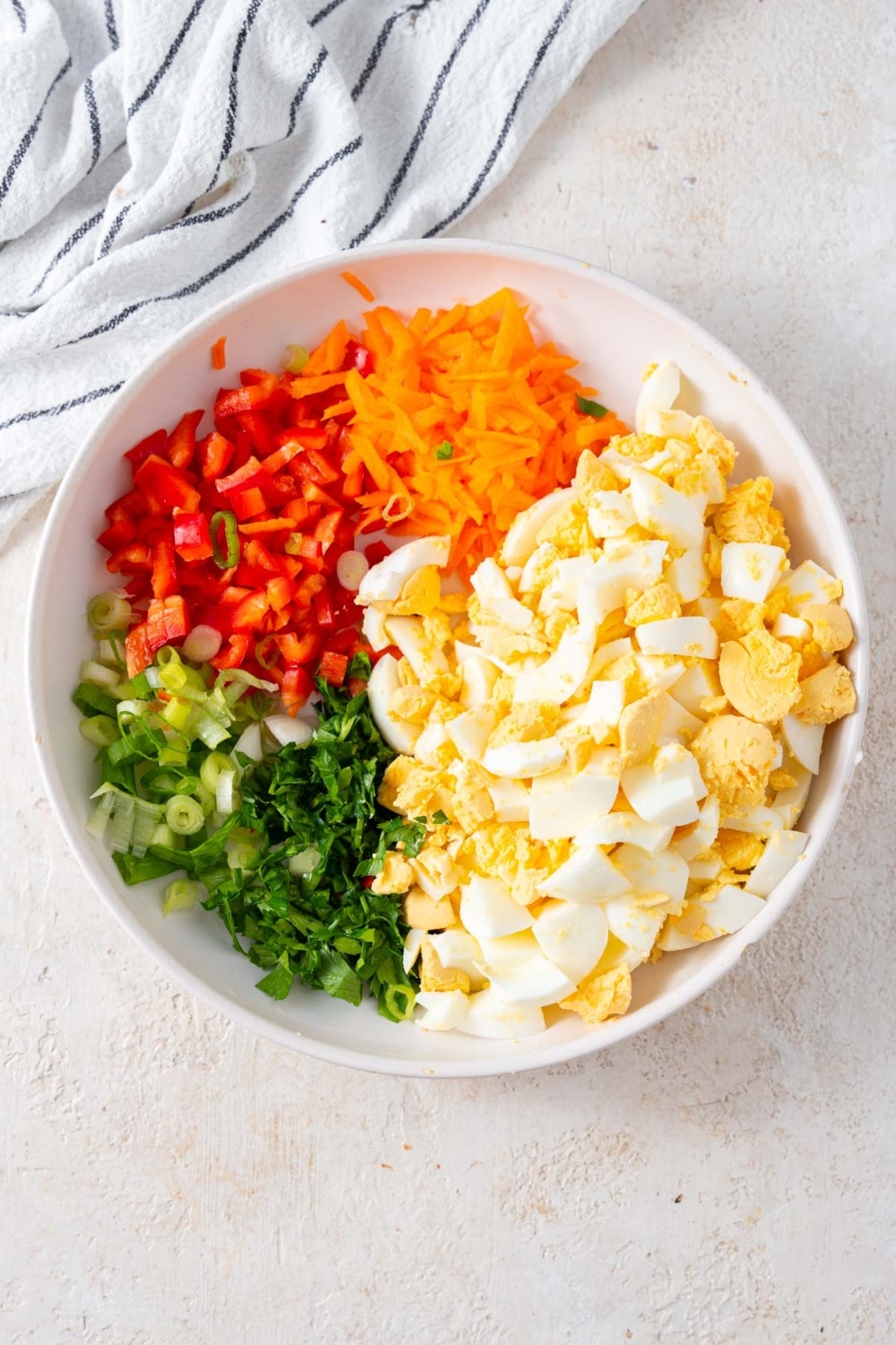 A bowl of chopped hard boiled eggs, grated carrot, diced bell pepper, chopped green onions, and chopper parsley.