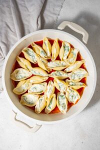 Unbaked cottage cheese stuffed pasta shells in marinara sauce in a pot.