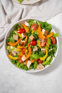 A bowl of chopped romaine lettuce, sliced bell peppers, sliced cherry tomatoes, and diced cooked chicken breast.