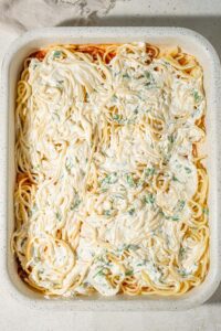 Spaghetti topped with creamy baked spaghetti filling in a casserole dish.