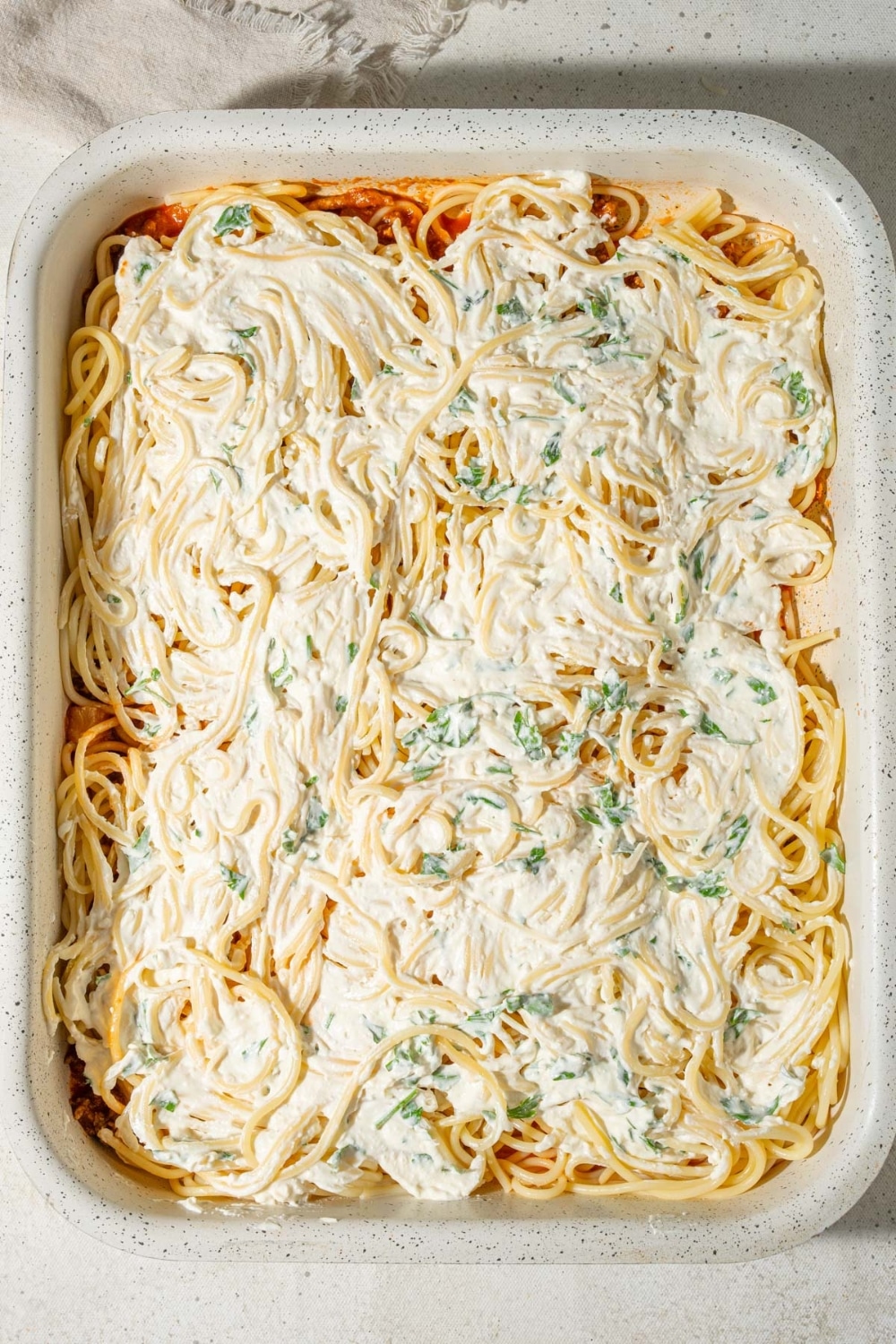 Spaghetti topped with creamy baked spaghetti filling in a casserole dish.