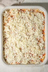 Spaghetti topped with shredded mozzarella cheese in a casserole dish.