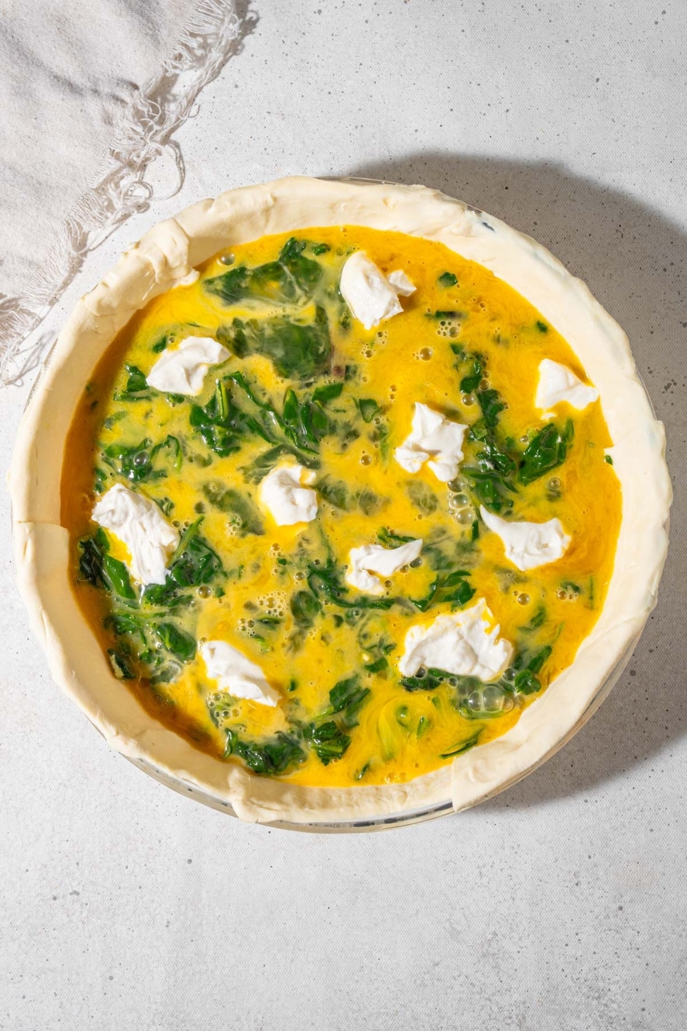 Uncooked spinach quiche with dollops of whipped cottage cheese.