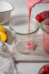 Pouring strawberry cottage cheese smoothie into a glass next to another smoothie.