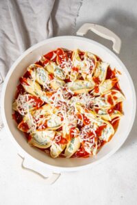 An unbaked pot of cottage cheese stuffed shells in marinara sauce topped with shredded mozzarella cheese.